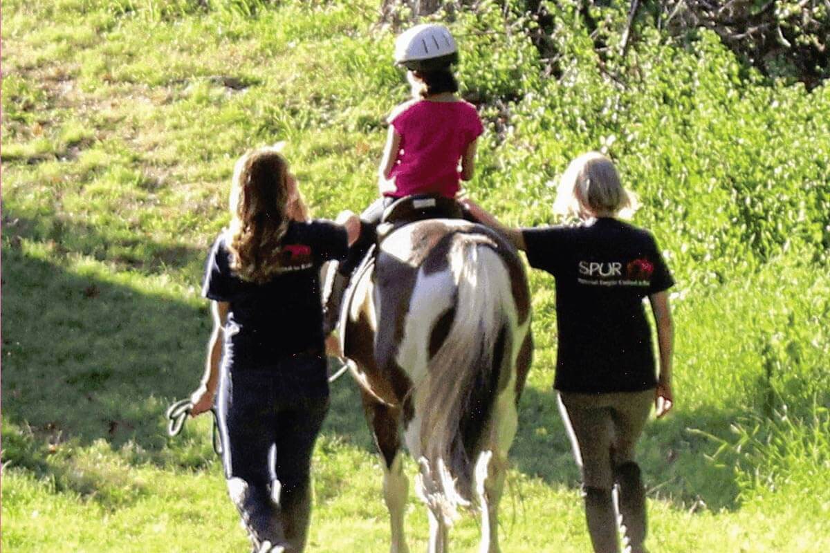 SPUR employees helping child ride a horse