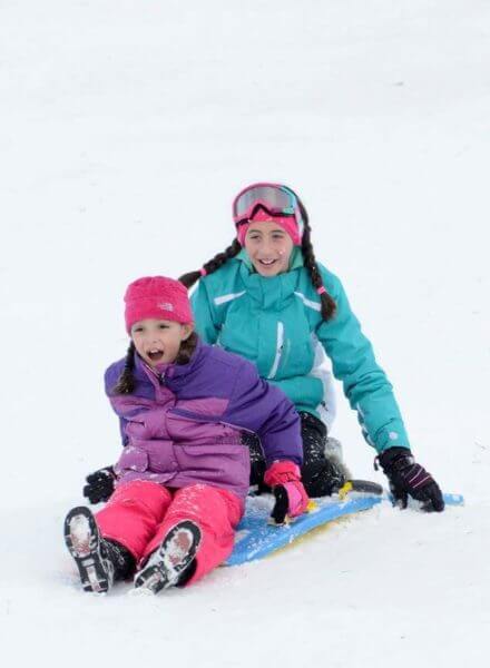 Two little girls sledding down now slope