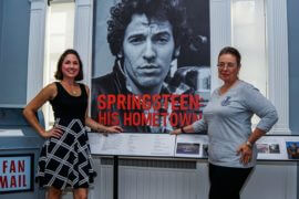 2 women posing in front of Springsteen: His Hometown, sign