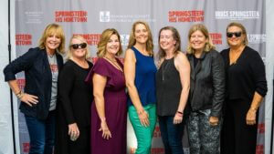 7 women posing in front of Springsteen: His Hometown, curtain