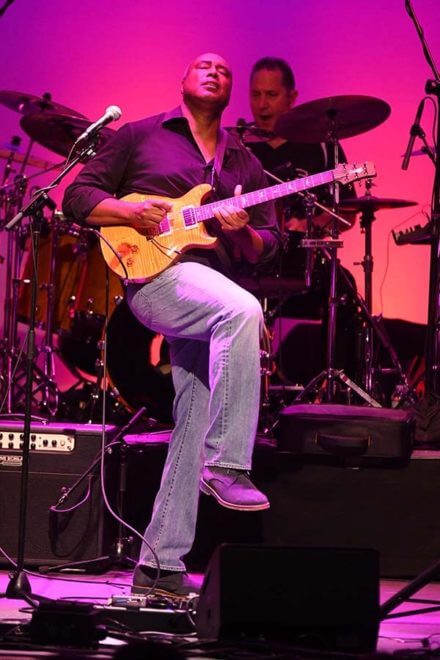 Bernie Williams playing guitar on stage, purple background